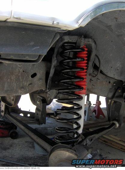 Close-up of a truck's front suspension with a new coil spring and red shock absorber boot