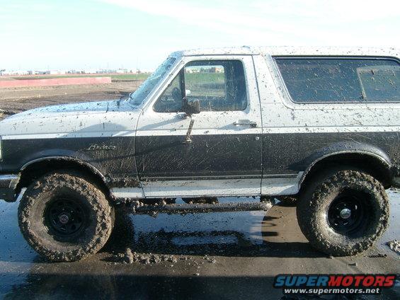 Mud-splattered white and black Ford Bronco, side view, with off-road tires