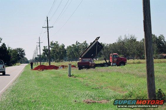 Dump truck with raised bed next to a red pickup truck on a grassy field with power lines
