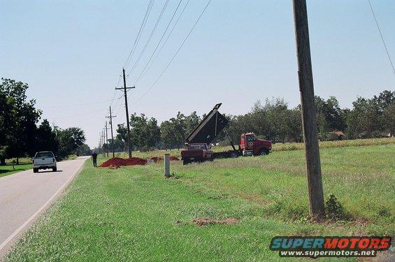 Dump truck with bed raised next to a pickup truck on a grassy field with power lines overhead