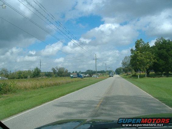 driving down a rural road with power lines overhead, two trucks visible in the distance