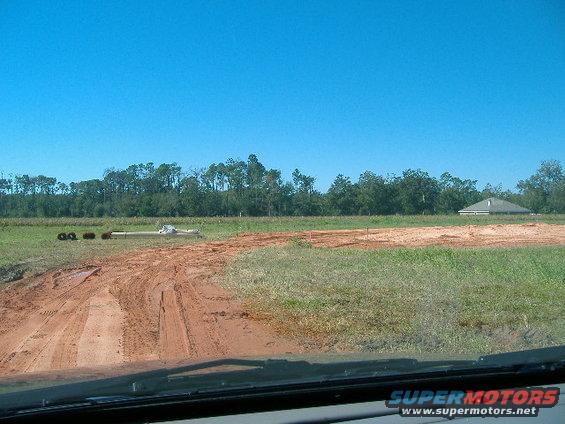 Dirt road through a grassy field under a clear blue sky
