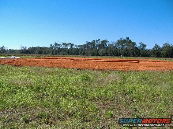 Construction site with cleared land and dirt mounds, trees in background under a clear blue sky