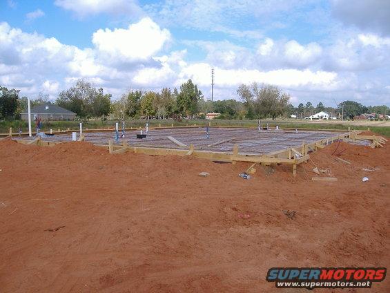 Construction site with concrete foundation and plumbing pipes under a cloudy sky