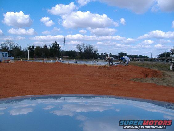 Construction site with a van and workers, reflection of clouds on car hood