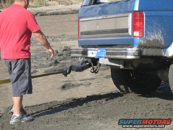 1987 Ford Bronco rear bumper and taillight in mud, man pulling with strap