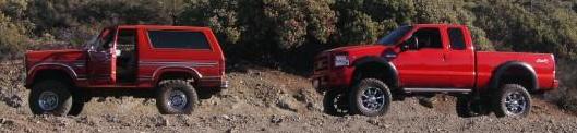 Side view of a red 1986 Ford Bronco and a red pickup truck on a dirt hillside