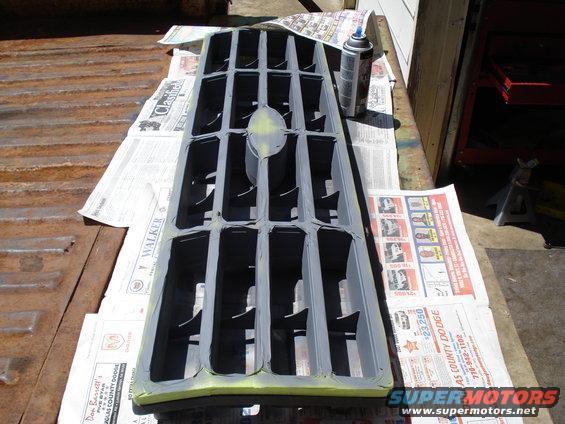Grille being prepped for paint, laid out on newspapers with a spray can nearby