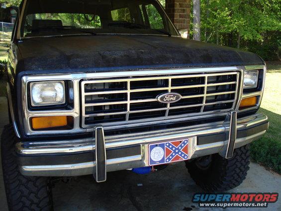 Front of a dark-colored Ford Bronco with a chrome grille and bumper. License plate has a Confederate flag design