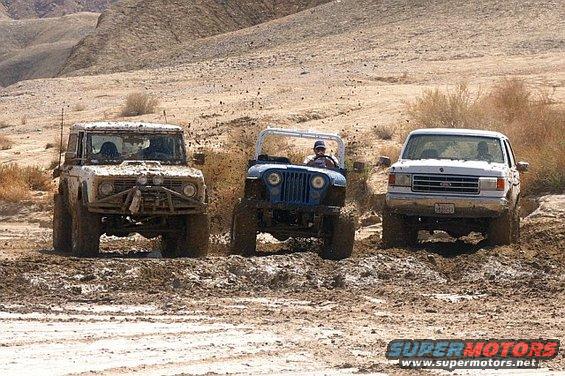 White 1990 Ford Bronco front view in mud, with blue Jeep and white pickup truck