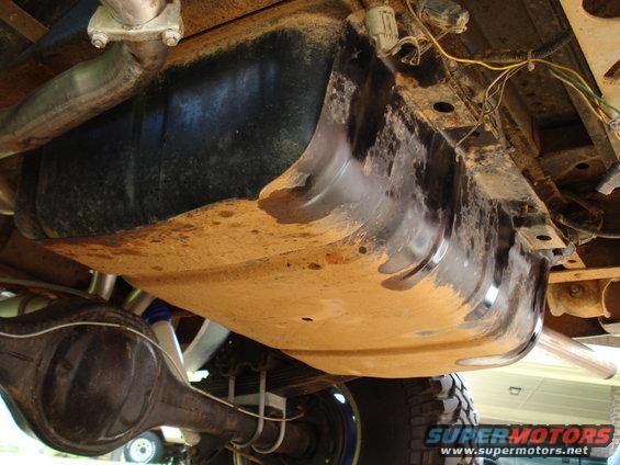 1984 Ford Bronco fuel tank and rear axle, viewed from underneath. The tank is black and appears dirty