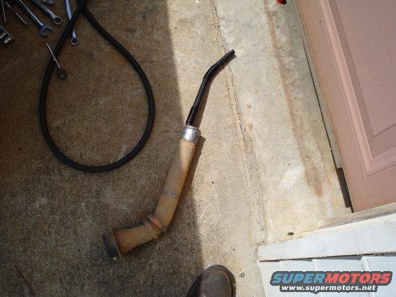 rusted exhaust pipe section with a black hose coiled nearby on concrete