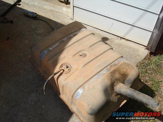 Rusty metal fuel tank with hoses and a can of spray paint on concrete