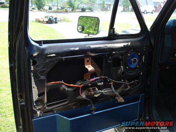Interior of a dark blue car door with removed panel, showing exposed wiring, speaker, and window mechanism