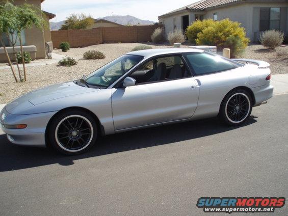 1997 Ford Probe coupe, silver, black aftermarket wheels, parked on asphalt in front of a house
