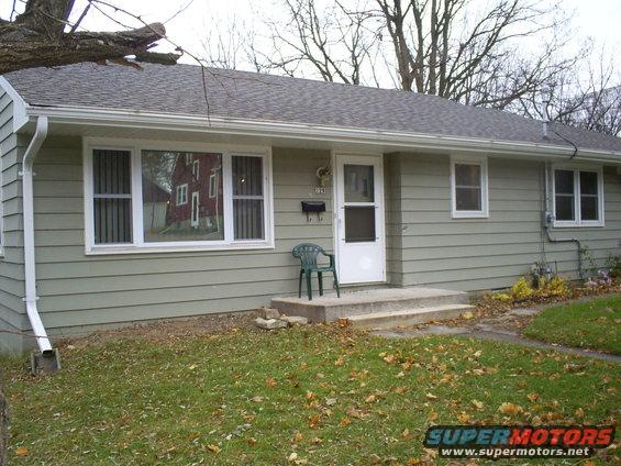 Light green house with white trim, front door, and windows. A green plastic chair sits on the concrete steps