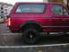 1994 Ford Bronco - Side profile of a red 1994 Ford Bronco parked in a lot with fallen leaves.