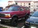 1994 Ford Bronco - A lifted red 1994 Ford Bronco is parked in a lot next to a black BMW.