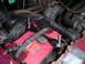 1994 Ford Bronco - The engine bay shows a red Optima battery secured with metal brackets and bolts, surrounded by hoses and an alternator.