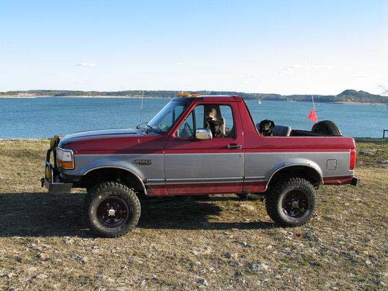 Red and silver two-door SUV with two dogs in the cab, parked by a lake