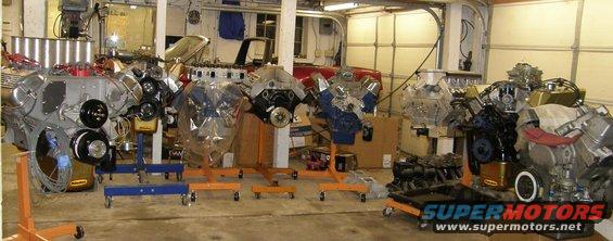 Several V8 engines displayed on engine stands in a workshop setting. Some engines are partially covered