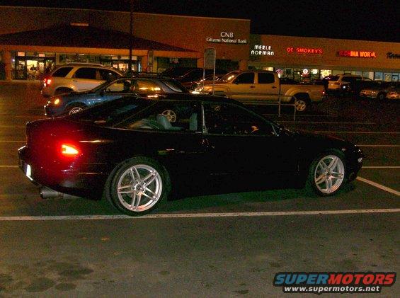 Black coupe with aftermarket wheels parked at night in a parking lot