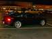 1995 Ford Probe - A black coupe is parked in a lot at night, with other vehicles and businesses in the background.