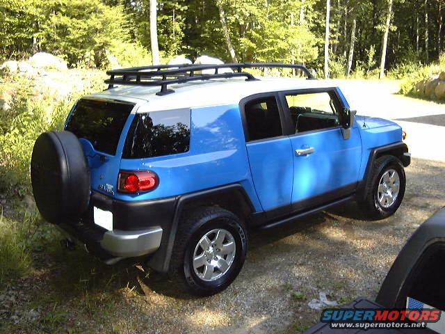 Blue Toyota FJ Cruiser parked outdoors, spare tire on rear door, roof rack installed