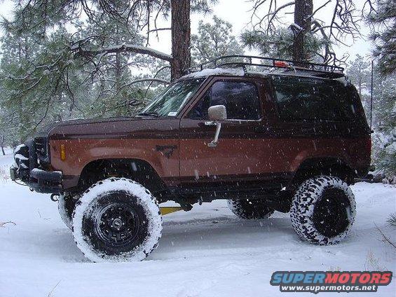 Brown Ford Bronco with roof rack and large tires in snow