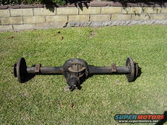 Rear axle assembly on grass, with brick wall in background. Shows differential housing and axle tubes