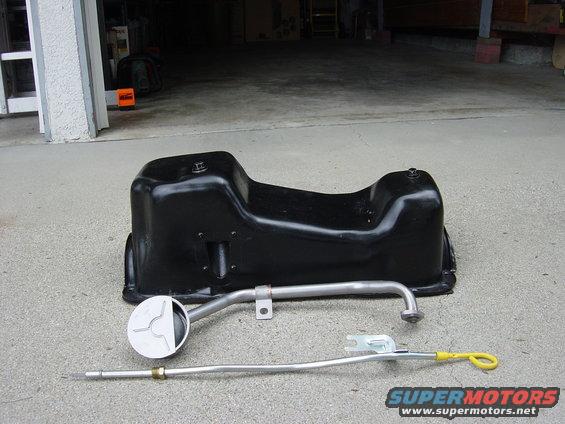 Black oil pan and metal dipstick with yellow handle on concrete