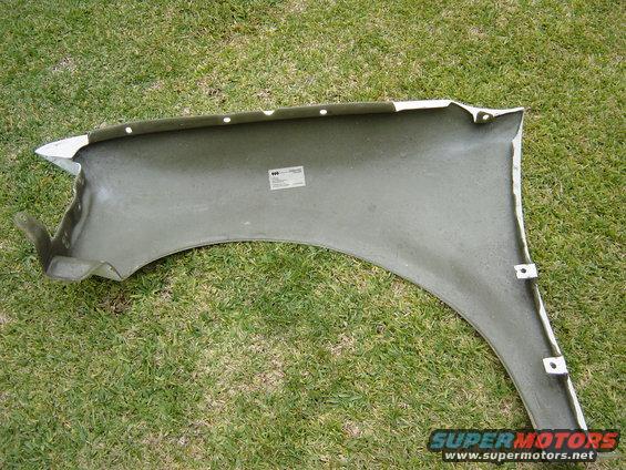 Inside of a white car fender, possibly fiberglass, lying on grass. Has a sticker on the inside