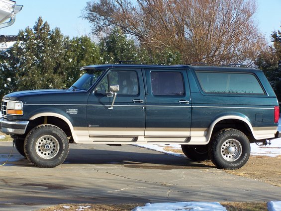 Side view of a dark green and tan extended cab pickup truck with a camper shell