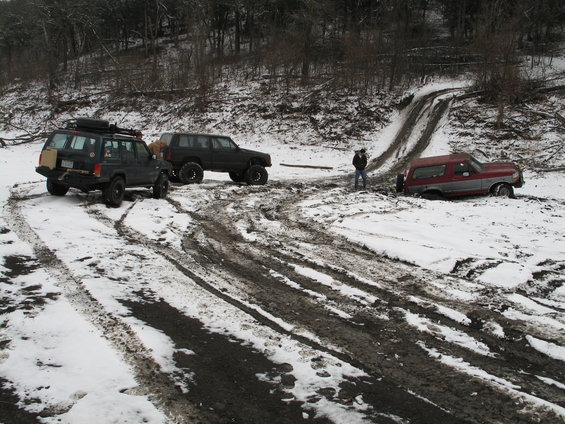 Red and silver Ford Bronco stuck in mud and snow, 3/4 front view