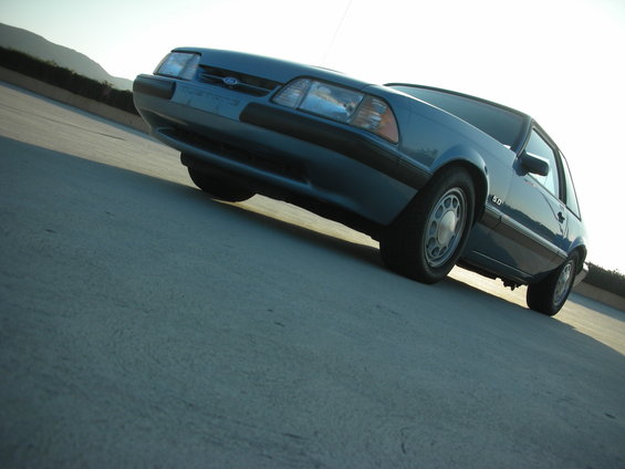 Blue 1990 Ford Mustang parked on a concrete surface with hills in the background