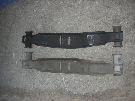 two car suspension control arms, one black and one gray, on concrete