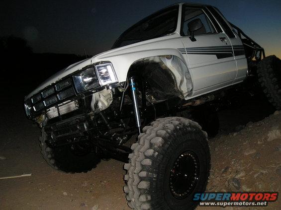 White 1986 Toyota Hilux with large off-road tires and suspension lift
