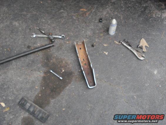 Tools and a metal bracket are scattered on a concrete surface