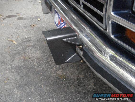 Close-up of a custom black metal bracket bolted to the chrome bumper of a truck, with a partial grille and license plate visible