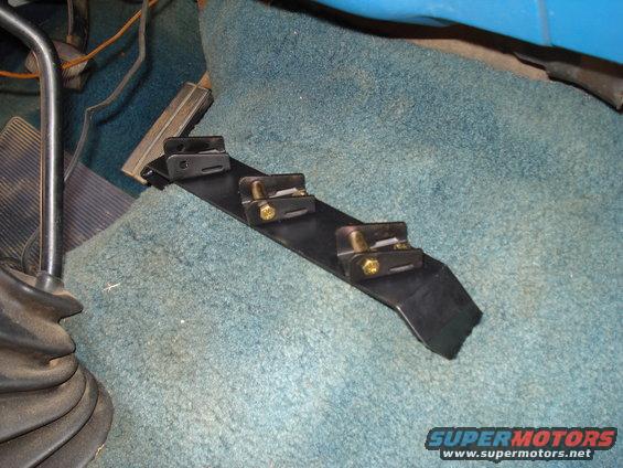Black metal bracket with three gold-bolted clamps on blue carpeted floor