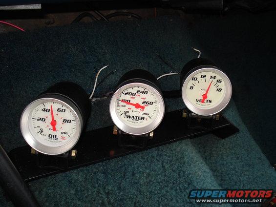 Three dashboard gauges mounted on a black plate: oil pressure, water temperature, and voltage