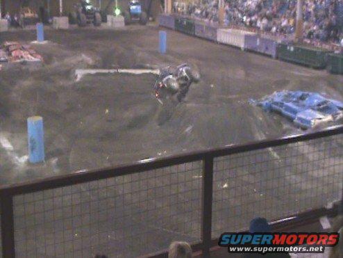 Monster truck upside down on dirt track with spectators in background