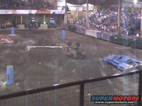 Monster trucks compete in an indoor arena with spectators in the stands