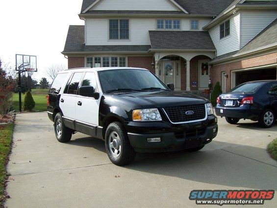 Ford Expedition with black front and white rear doors parked in driveway. Blue sedan in garage