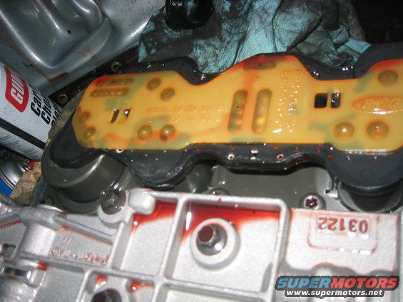Transmission valve body with red fluid and a yellow circuit board. A can of car cleaner is visible on the left