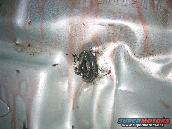 Close-up of a transmission pan with a bolt and some red fluid drips