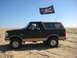 1994 Ford Bronco - A black 1994 Ford Bronco with a tan top cruises over sand dunes, flying a pirate flag on a clear day.