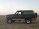 1994 Ford Bronco - A Ford Bronco with a two-tone paint job sits on a sandy beach with RVs in the background.