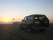 1994 Ford Bronco - A 1994 Ford Bronco is parked on the sand near the ocean as the sun sets, with a spare tire mounted on the rear door.