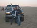1994 Ford Bronco - Two young men pose in front of a black Ford Bronco in a sandy, desert-like environment with a quad bike in the distance.